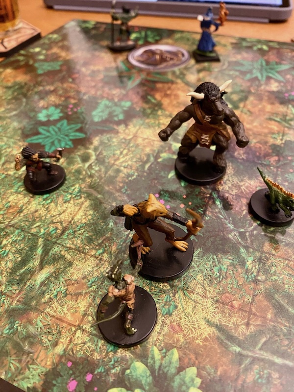 Minis on jungle battle mat. Minotaur, gnome, kobold & velociraptor surround a tabaxi with a bow
