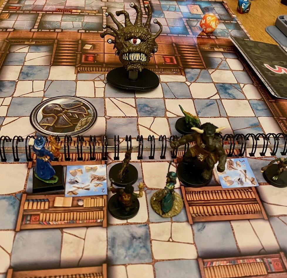 PC minis and shield guardian counter fighting a beholder mini and paper golem swarms on a library battle map.