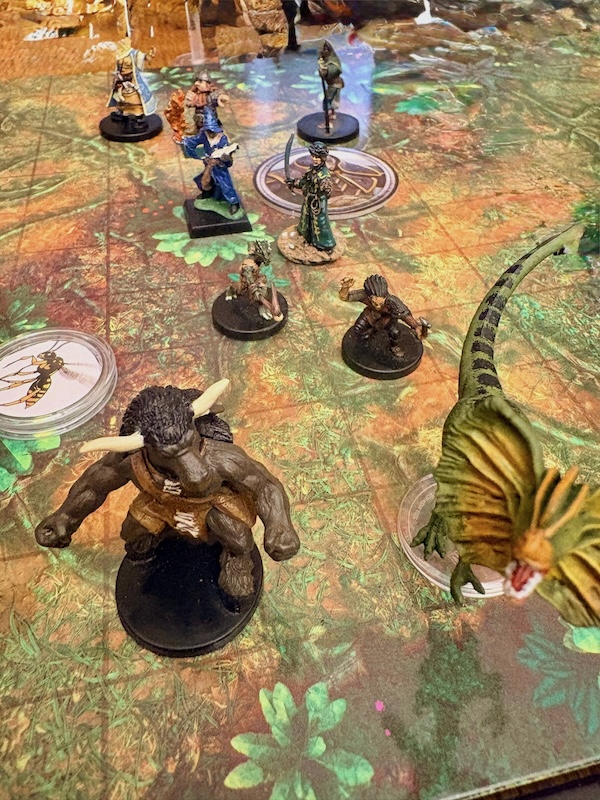 PC & animal companion miniatures on jungle battle mat. Minotaur & dinosaur in foreground.