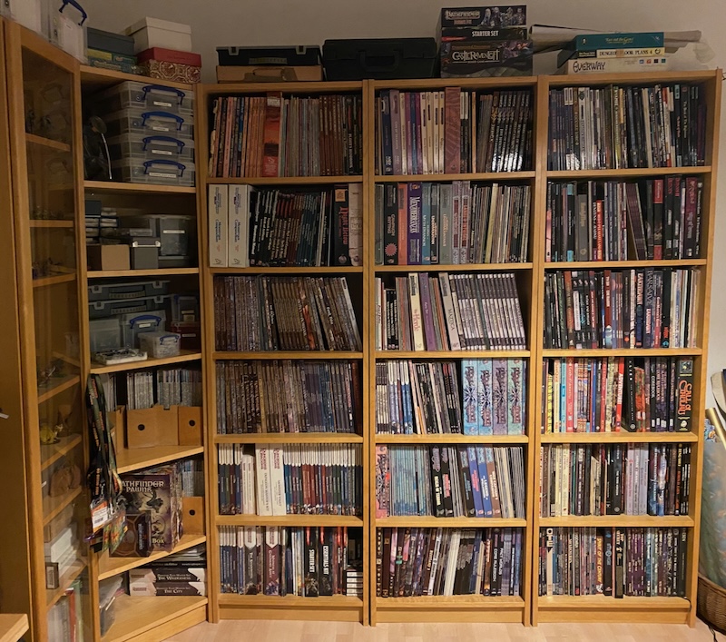 Bookcases filled with RPG books, minis, dungeon tiles, magazines etc