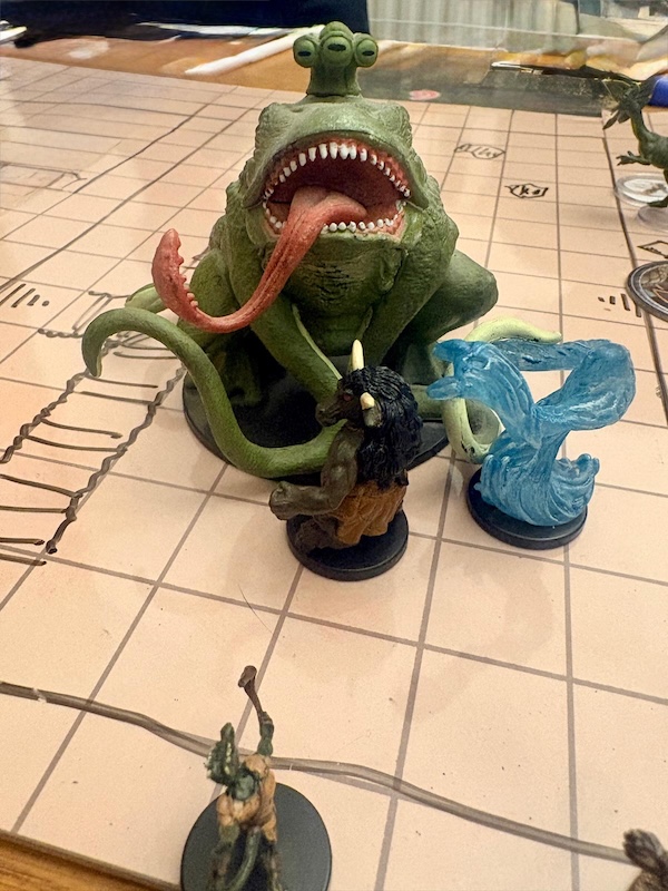 Huge froghemoth mini fighting minotaur, water elemental and kobold monk on a hand drawn battle map