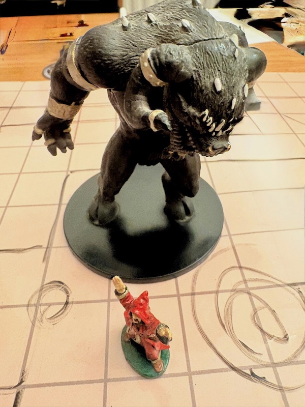 Towering ape-like demon mini attacks tiny red wizard on hand-drawn battle mat