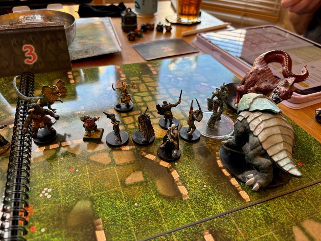 Two large dinosaur minis and assorted PC minis in combat on a ruins battle map